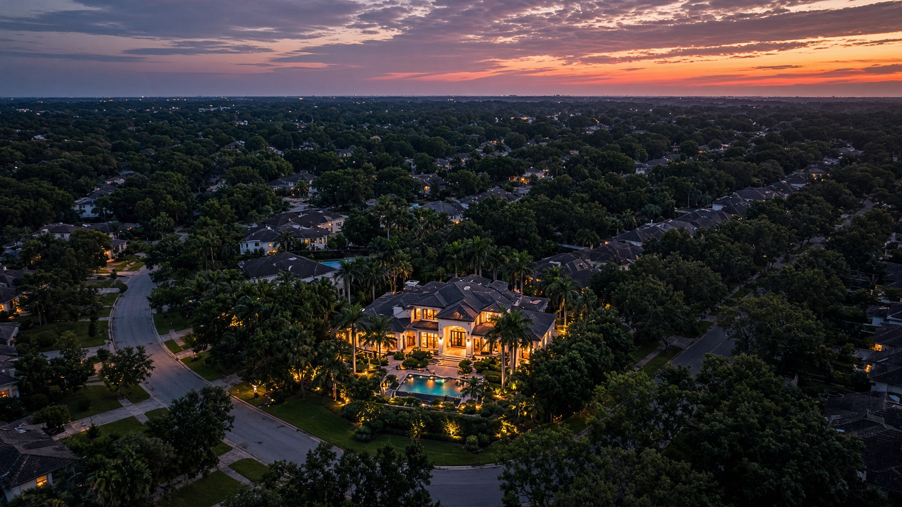 Aerial neighborhood at dusk with the featured home glowing at center