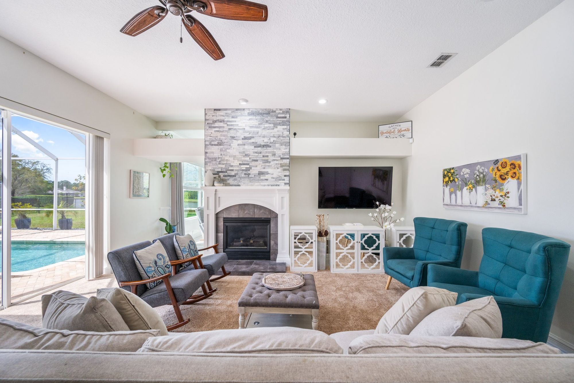 Living room with a stone fireplace and the pool beyond