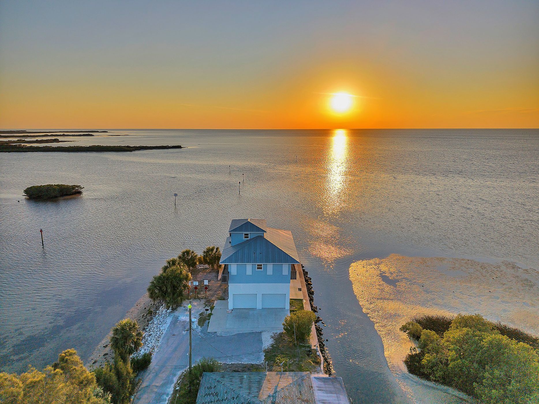 Drone view of the house facing the sunset over open water